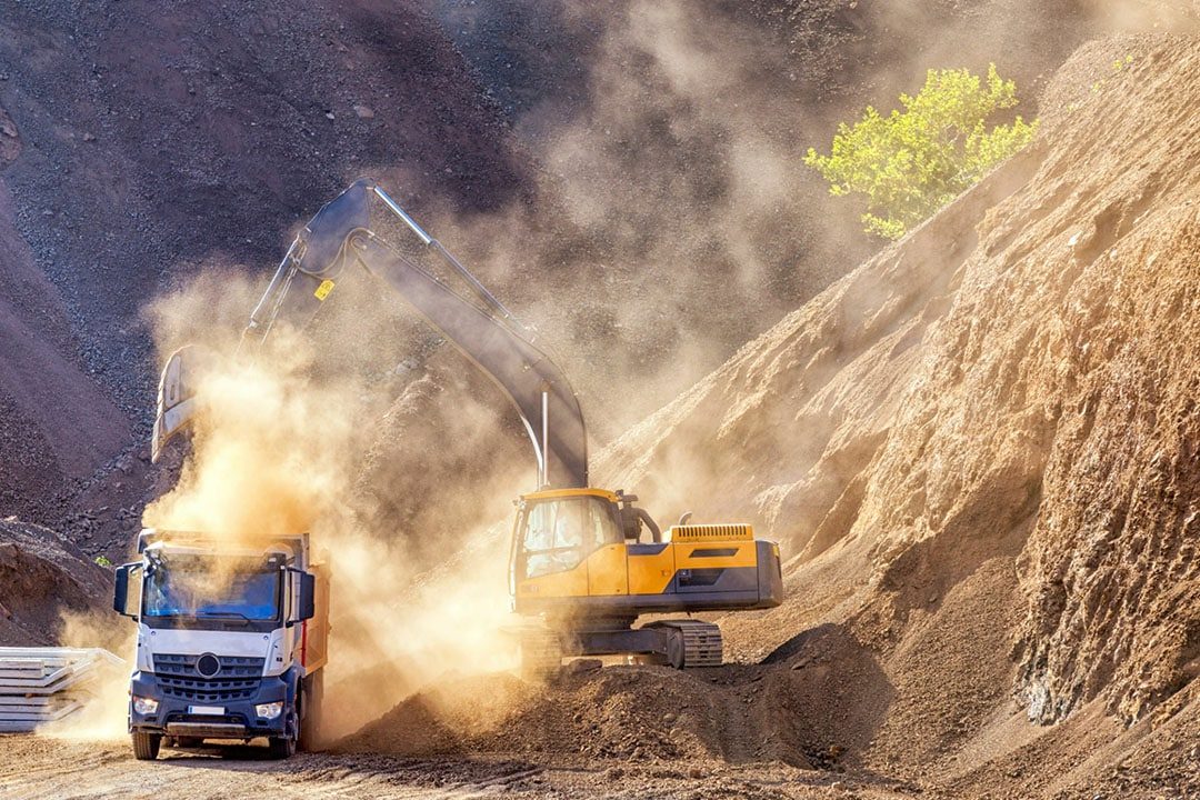 Pelleteuse chargeant un camion-benne dans un nuage de poussière